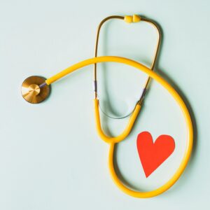 Medical stethoscope with red paper heart on white surface